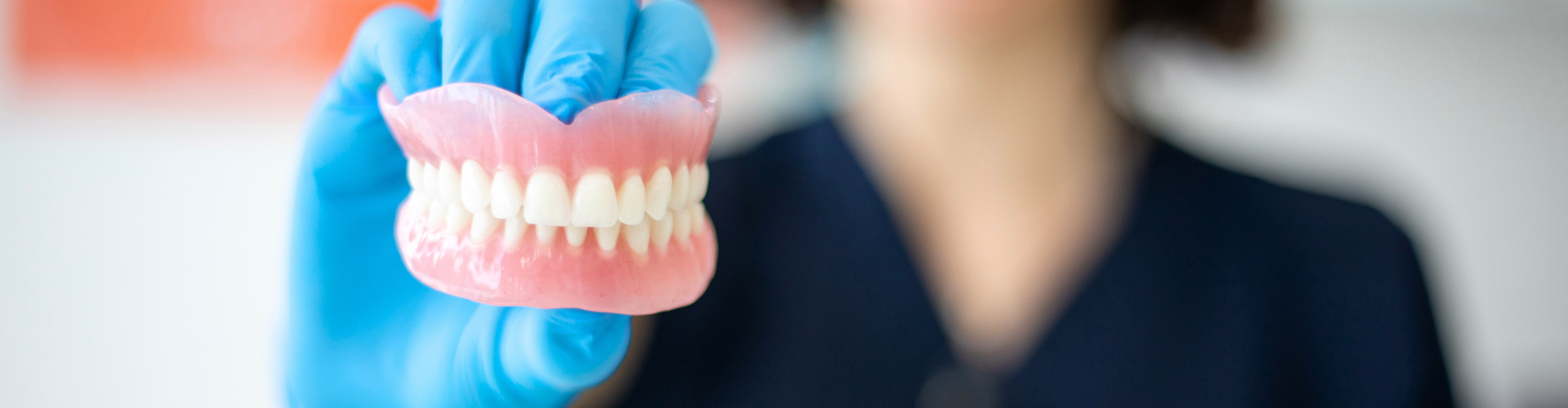 Smiling woman holding pair of dentures in gloved hand.